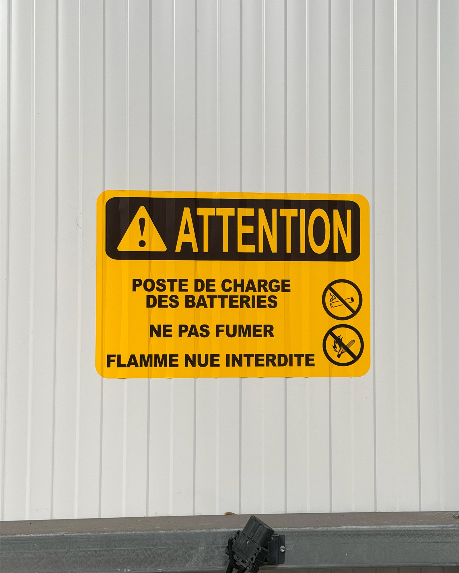 Panneau de sécurité jaune signalant les interdictions de fumer et d'utiliser une flamme nue près d'un poste de charge de batteries.